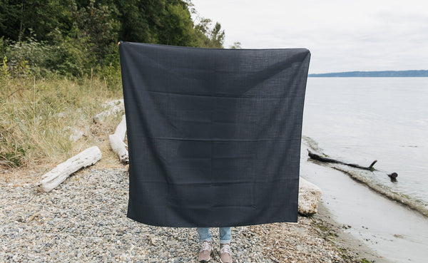 A person at the beach holding a Large Shepherd's Wool Utility Cloth in Matter Grey.